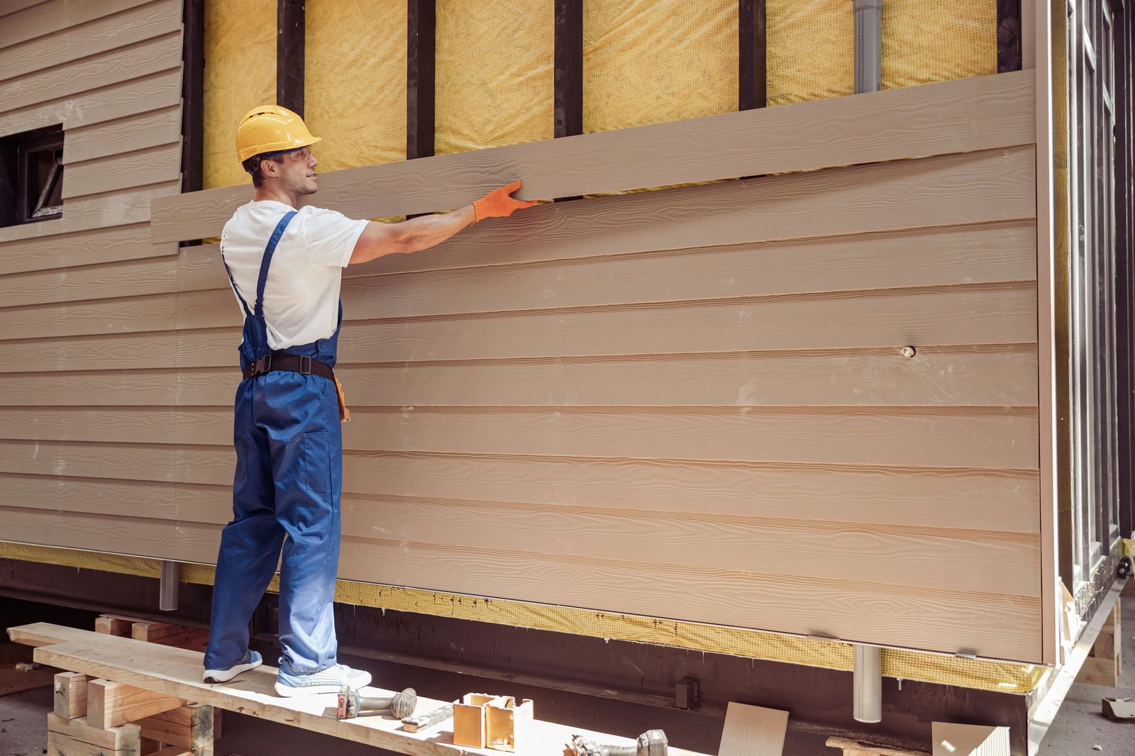 Contractor installing tan lap siding over insulation on a home under construction