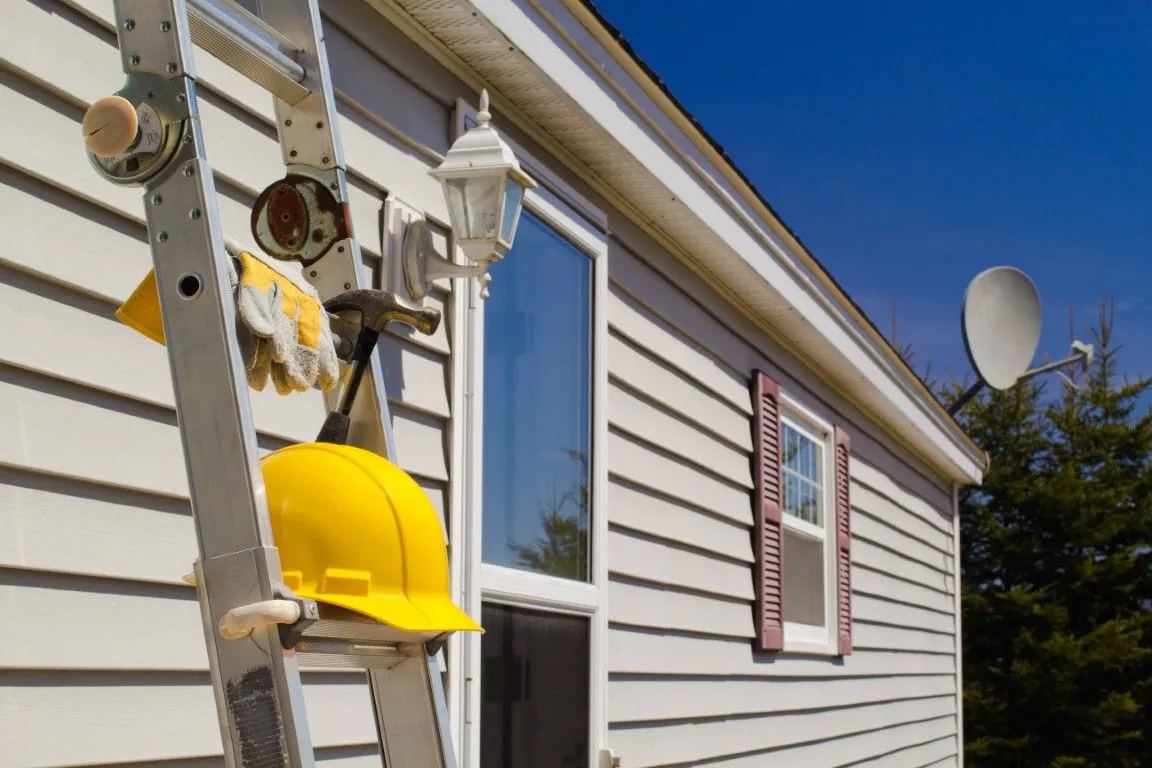 Ladder with tools and hard hat leaning against a vinyl-sided home