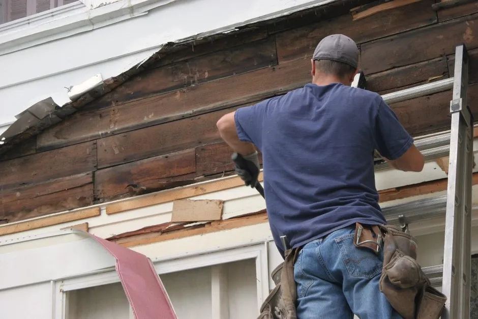 Worker removing old weathered wood siding during a full replacement